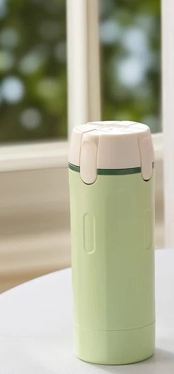 Green and beige thermos bottle on a light surface with a blurred window background