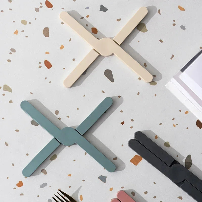 Three X-shaped coasters in beige, green, and black on a speckled surface.