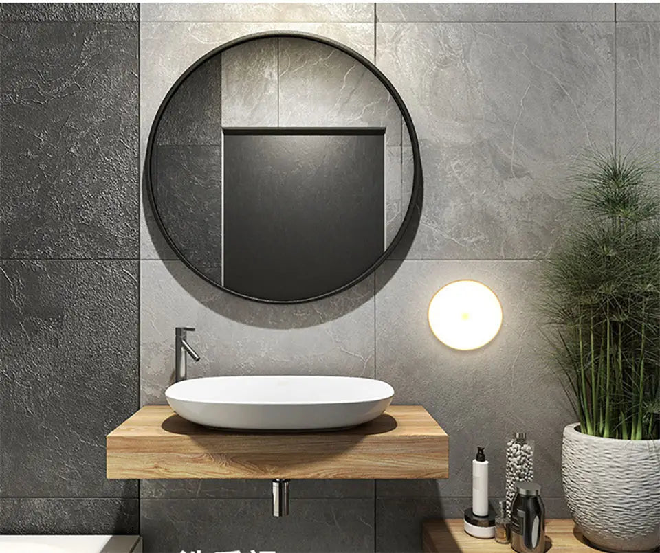 Bathroom with round mirror, sink, and decorative elements on a gray tiled wall.