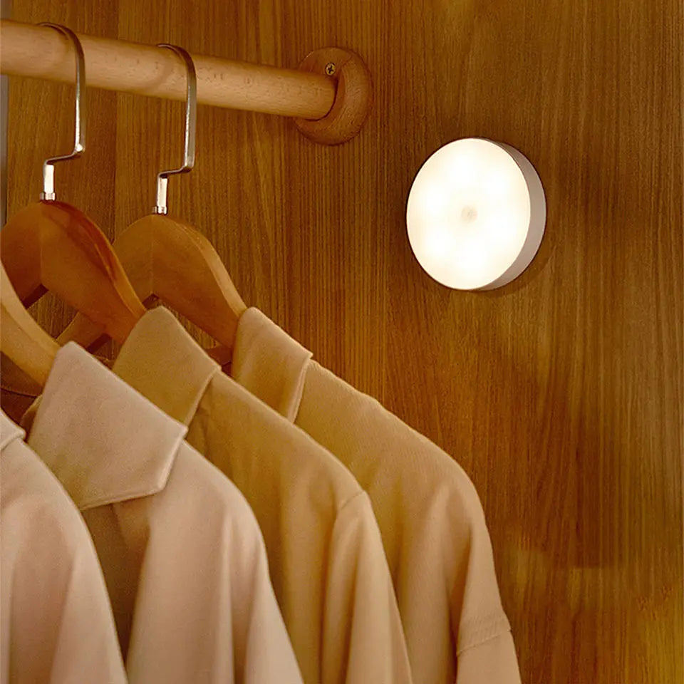 Round night light attached to a wooden wardrobe with hanging clothes.