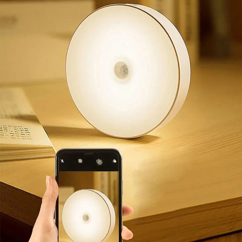 Round night light on a wooden surface with a phone taking a photo.