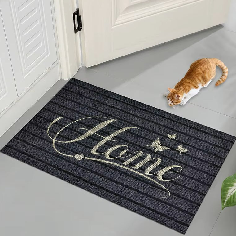 Black doormat with 'Home' text on a gray floor, cat nearby.