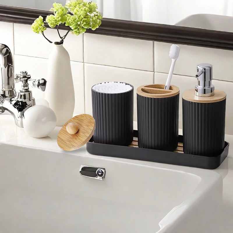 Bathroom counter with black and wooden toothbrush holders and a vase with green flowers.