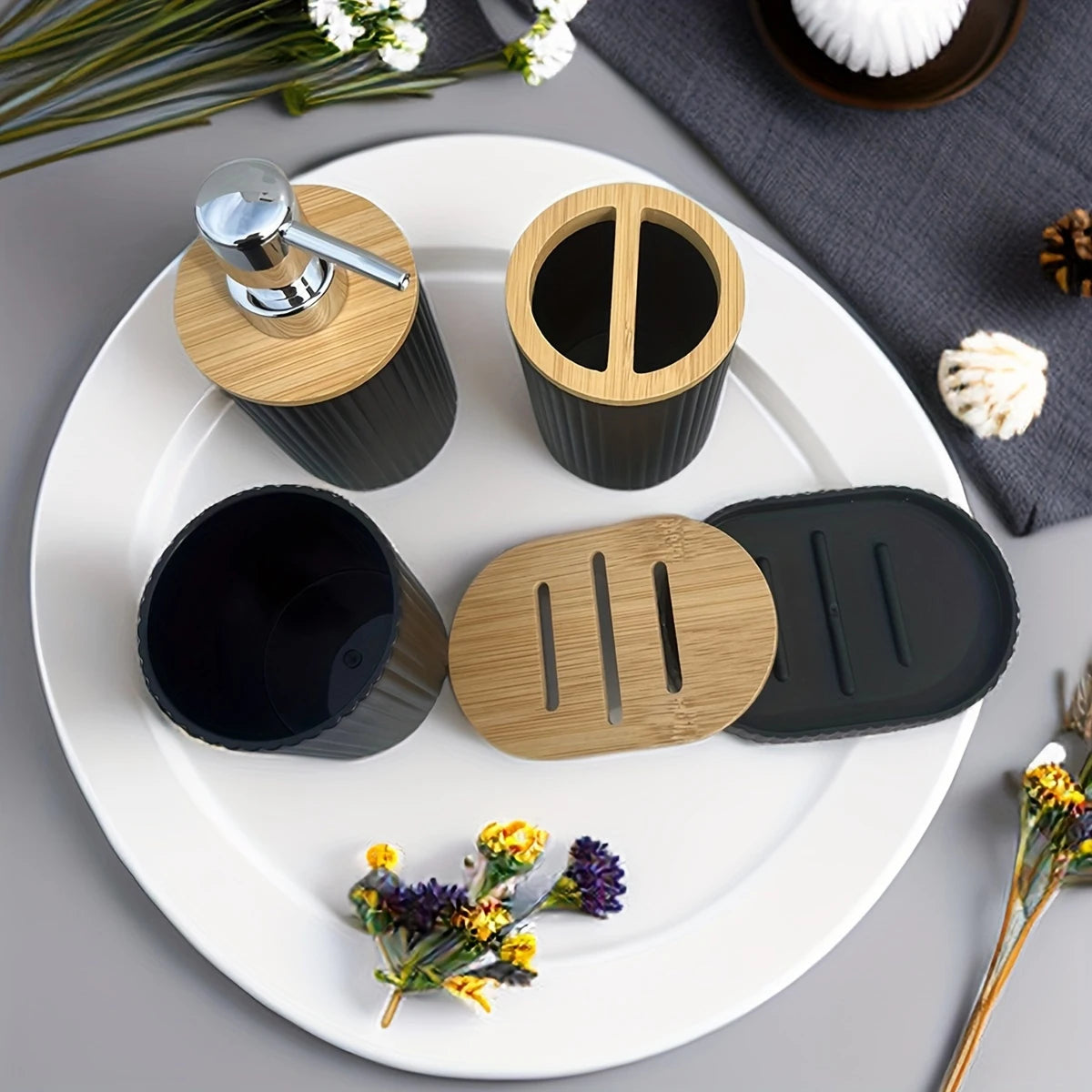 Bathroom accessories including a soap dispenser, black cups, and a soap dish on a white tray with flowers around.
