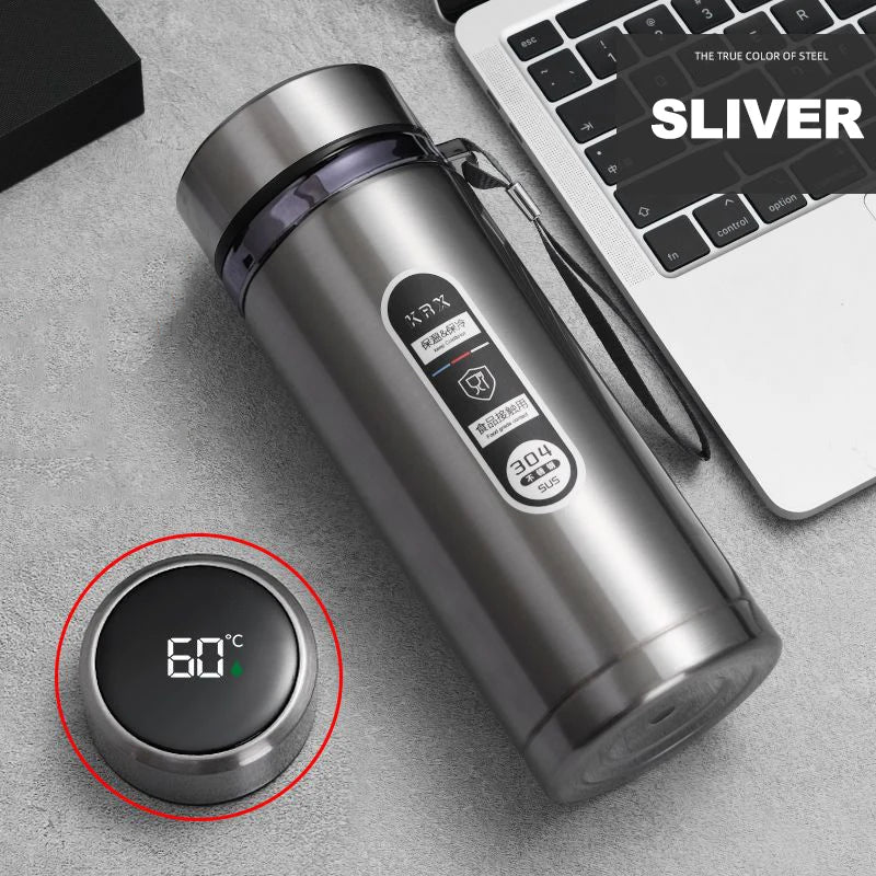 Silver thermos bottle with digital temperature display on a gray surface next to a laptop.