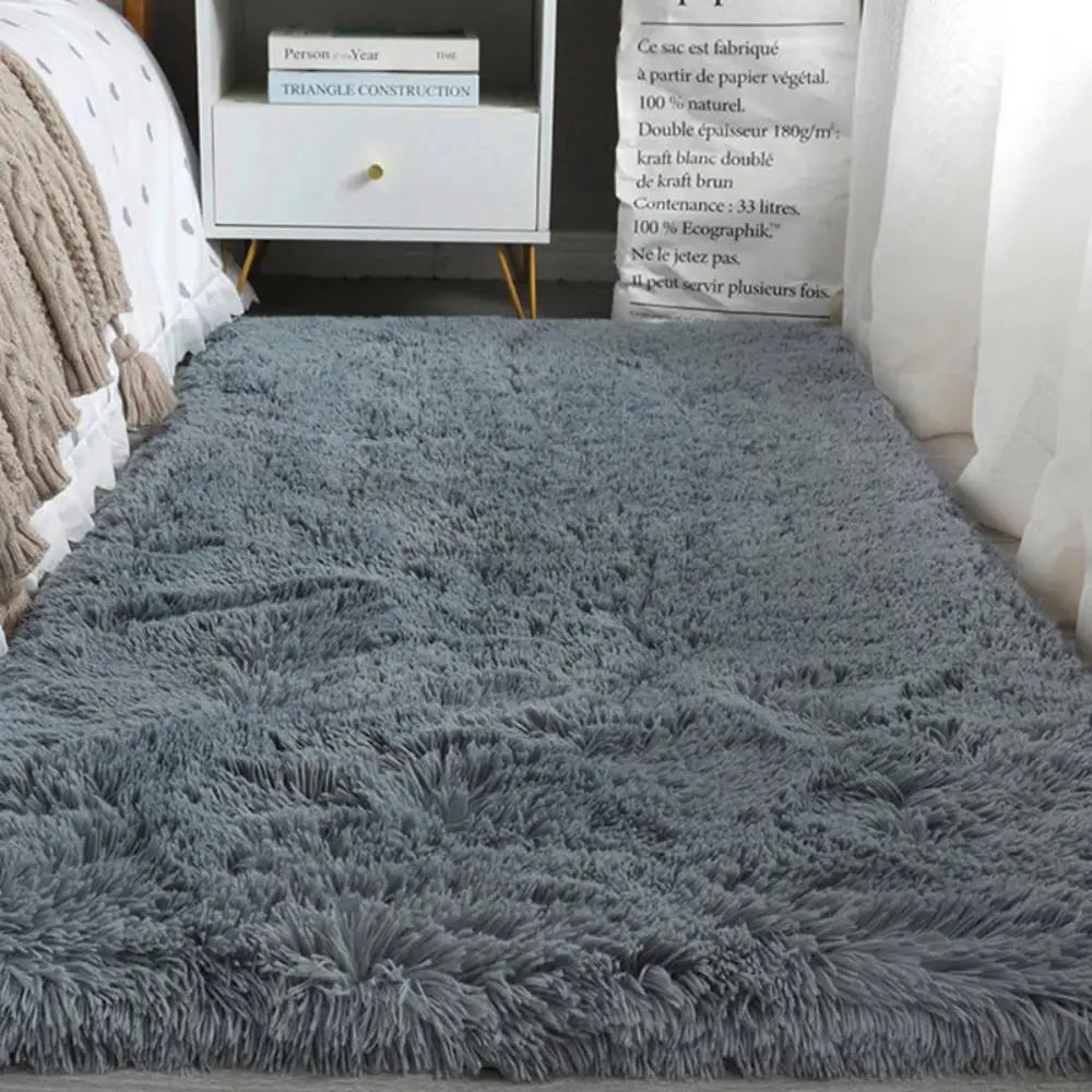 Gray shaggy rug on a wooden floor with a white chair and books in the background.
