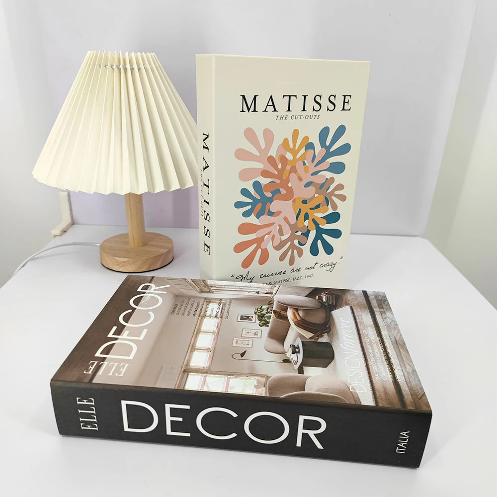 Two books titled 'Matisse' and 'Elle Decor Italia' on a surface with a lamp in the background.